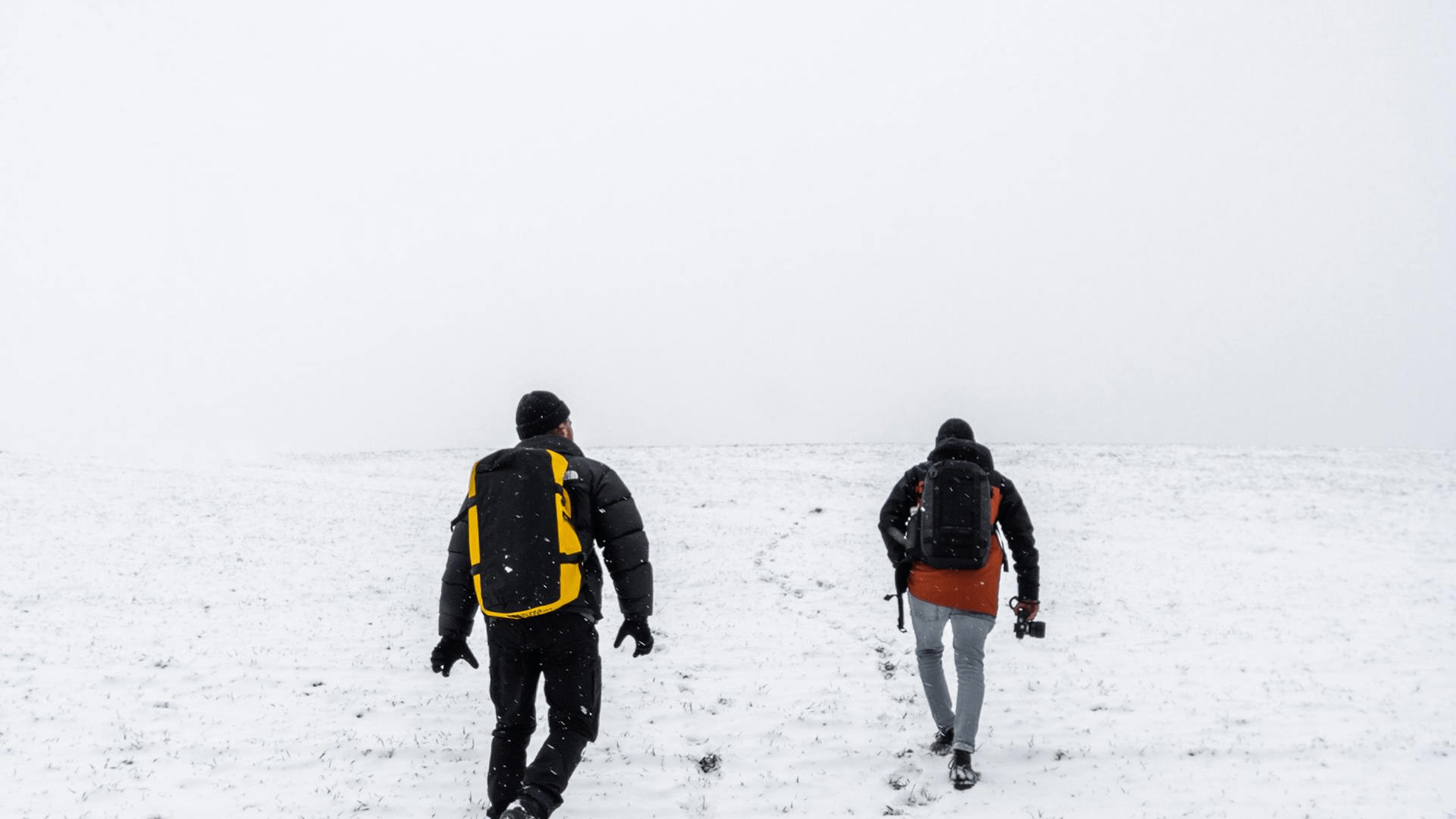 Deux trekkeurs de dos en train de marché sur un terrain de neige par temps de brouillard.