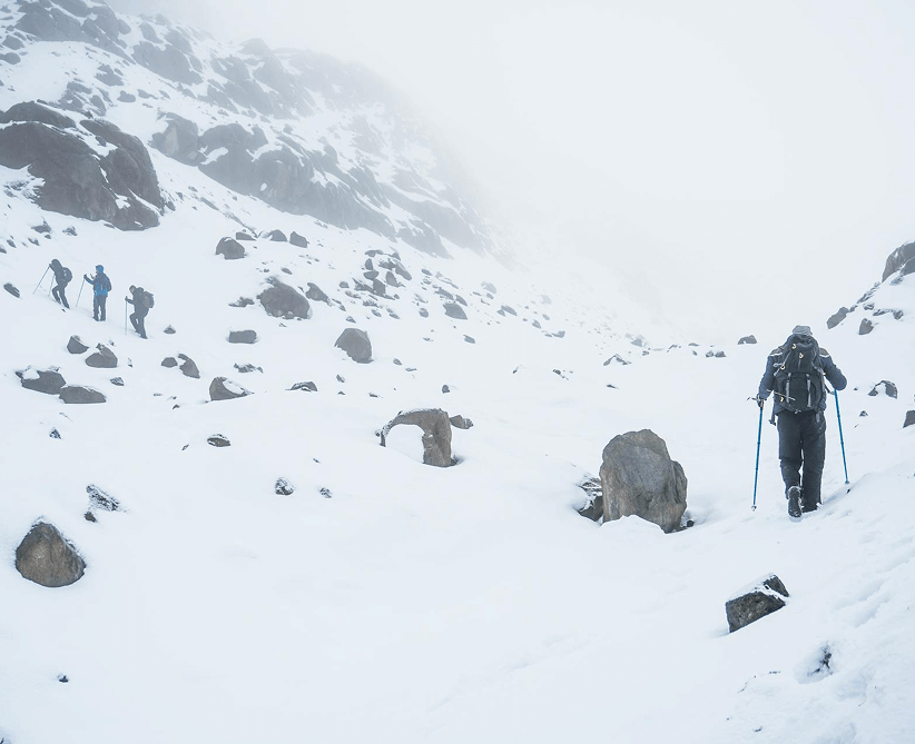 Un trekkeur marchant à l'aide de bâtons sur une pente enneigée par temps de brouillard.