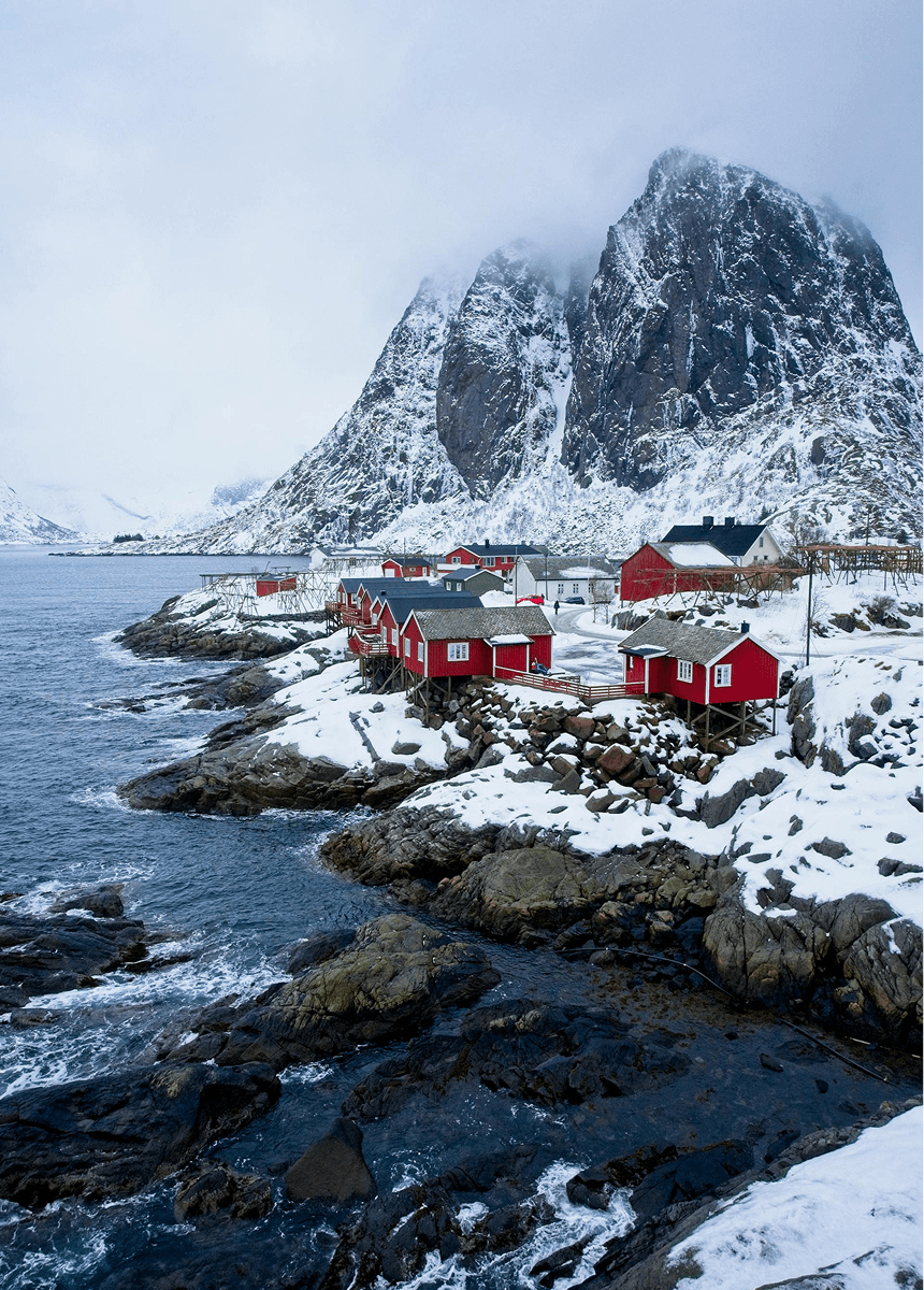 Des maisons rouges norvégiennes en bord de côte par temps de neige et de brouillard.